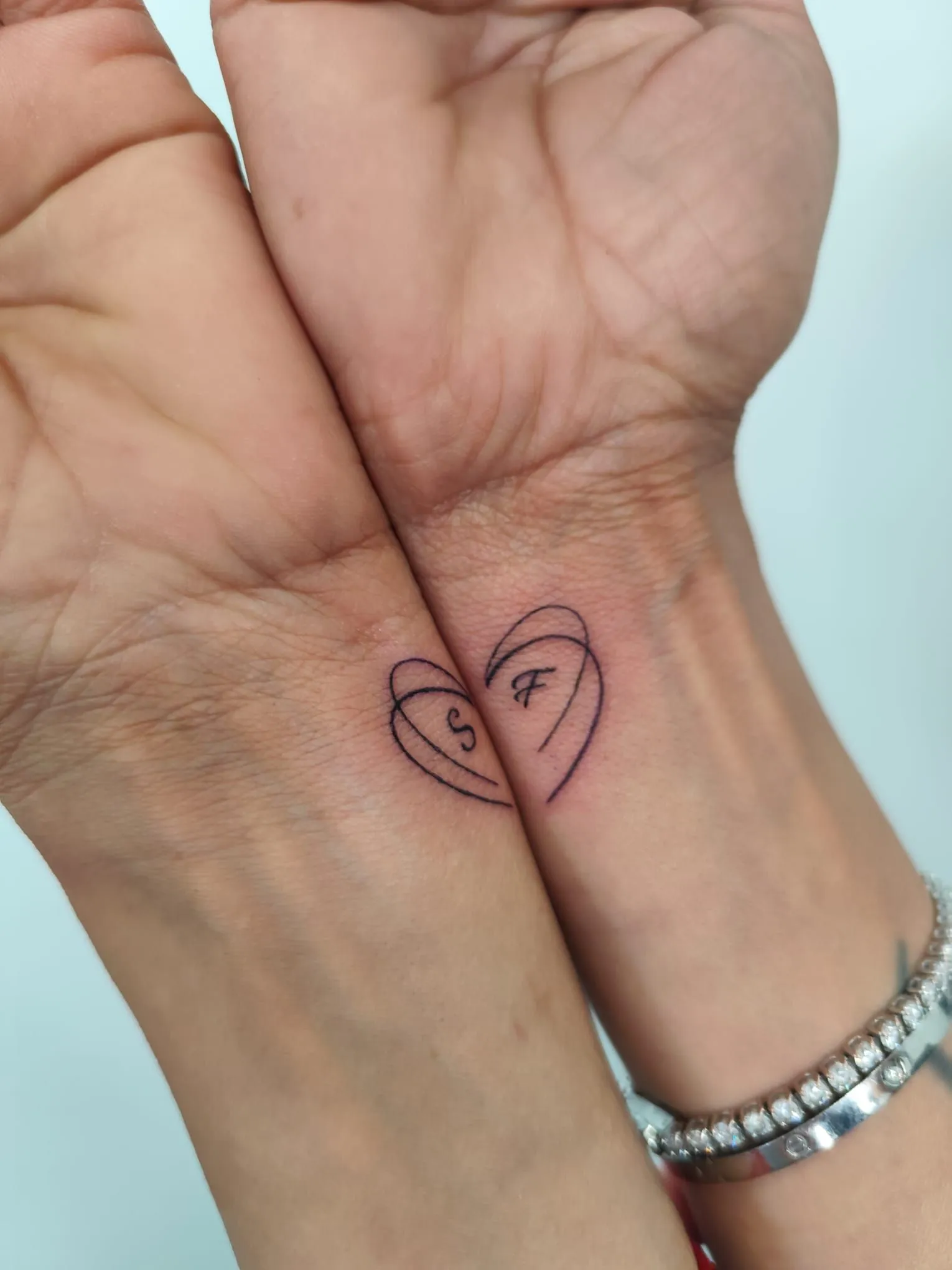 Dos manos entrelazadas con un pequeño corazón dibujado en la muñeca.