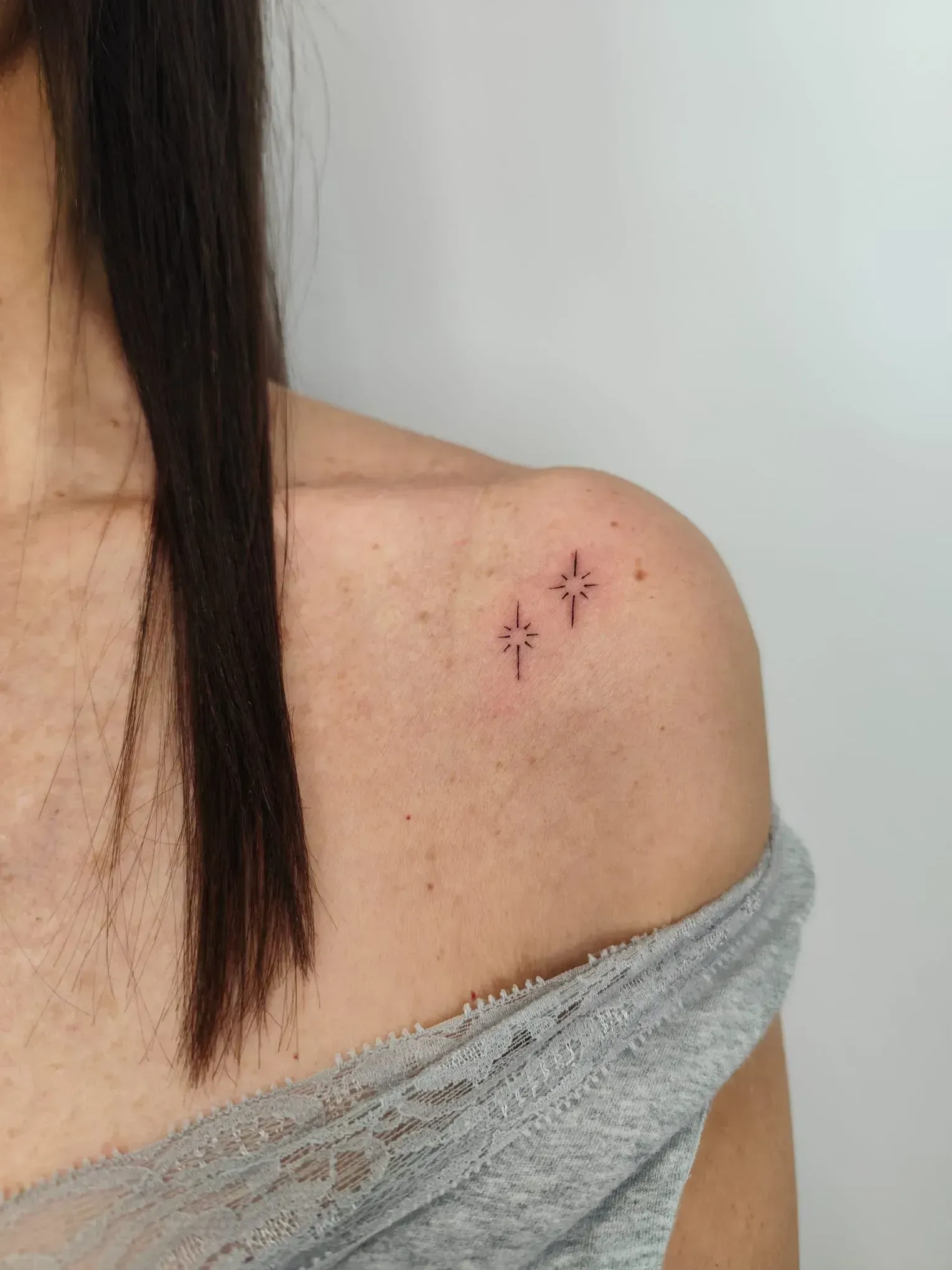 Hombro con tres pequeños tatuajes de línea fina cerca de la clavícula.